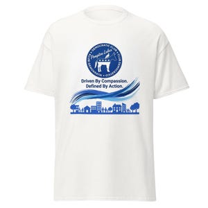 Può includere: T-shirt bianca con grafica blu e bianca. La grafica include un cerchio con testo e un asino, le parole "Driven By Compassion. Defined By Action" e una silhouette di paesaggio urbano.