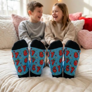 May include: A pair of blue socks with a repeating pattern of the numbers 6 and 7 in red, with hearts and green accents. The socks have black toes and heels. The socks are on the feet of two children.