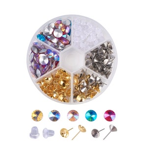 May include: A clear plastic container with six compartments filled with various earring supplies. The compartments contain gold-toned earring posts, silver-toned earring posts, clear earring backs, and a variety of colorful rhinestones.