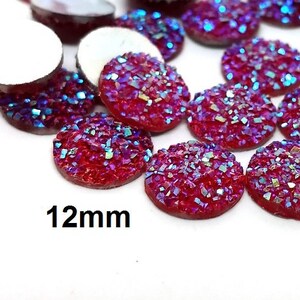 May include: A group of 12mm round, flat-backed, iridescent pink glitter cabochons. The cabochons have a holographic finish and are perfect for crafting projects.