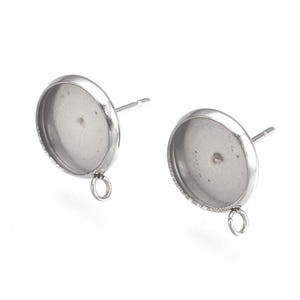 May include: A pair of silver earring settings with a round, clear glass bezel and a silver loop on the bottom. The earring posts are silver.