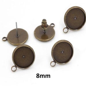 May include: A set of five round bronze-toned earring settings with an 8mm diameter. Each circular bezel features a small loop at the bottom for attaching charms or dangles, and includes a post backing for secure placement on the earlobe.