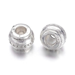 May include: Two silver metal bead spacers with a decorative design. The beads have a round shape with a hole in the center.