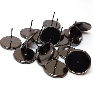 May include: A group of black metal earring settings with posts. The settings are round and have a smooth, shiny finish.