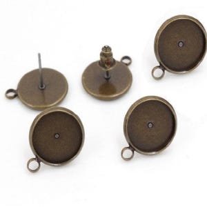 May include: Five antique bronze-colored earring components. The components include four round bezel settings with loops and one earring post with a flat round base. The components are for jewelry making.