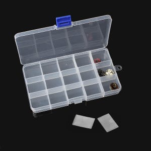 May include: A clear plastic organiser box with a blue clasp, divided into multiple compartments. Some compartments contain small, colourful beads. The box is open, revealing the contents, and two small, clear plastic rectangles are in front.