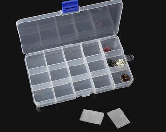 Op de afbeelding: Een doorzichtige plastic organizerbox met een blauwe sluiting, verdeeld in meerdere compartimenten. Sommige compartimenten bevatten kleine, kleurrijke kralen. De doos is open en onthult de inhoud, en twee kleine, doorzichtige plastic rechthoeken liggen ervoor.