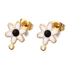 May include: A pair of gold-tone earrings featuring a white enamel daisy design with a black centre. The earrings have a small loop on the bottom for attaching charms.