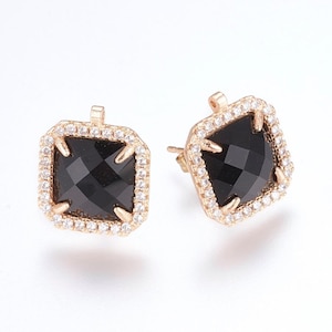 May include: A pair of gold earrings with black square-shaped gemstones surrounded by a halo of small clear stones.