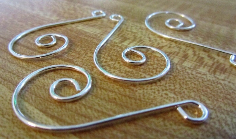 K&ouml;nnte beinhalten: Vier silberne Draht-Ornamentenaufh&auml;nger mit Spiraldesign. Die Aufh&auml;nger sind aus d&uuml;nnem Draht gefertigt und haben ein schlichtes, elegantes Design.