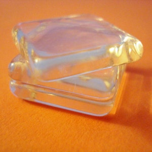 May include: Two clear glass boxes stacked on top of each other. The boxes are rectangular and have a slightly frosted appearance.