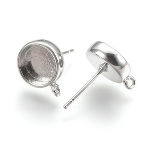 May include: Silver earring settings with a round bezel and a loop for attaching a charm. The settings are designed to hold a cabochon stone.