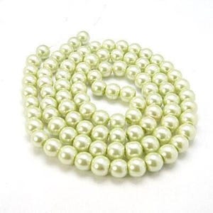 May include: A coiled strand of creamy, off-white faux pearls. The pearls are round and have a subtle lustre, reflecting light. The background is plain white, highlighting the necklace.