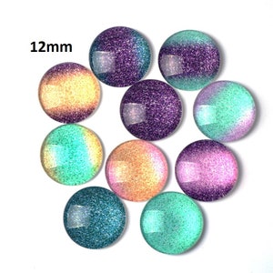 May include: Assortment of 12mm round glass cabochons with iridescent glitter. The cabochons feature a gradient of colors, including purple, pink, teal, and yellow.
