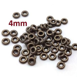 May include: A collection of small, bronze-coloured metal eyelets, each with a 4mm diameter. The eyelets are scattered on a white surface. The text "4mm" is displayed in red above the eyelets.