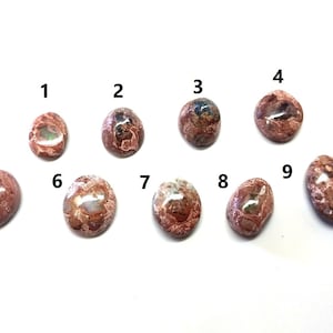 May include: Nine oval-shaped, pink and white opal cabochons with iridescent flashes. The cabochons are numbered 1 through 9.