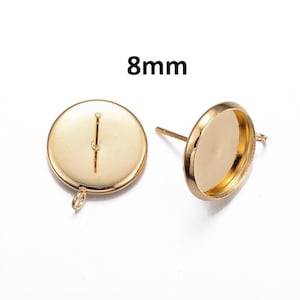 May include: Two gold-coloured earring posts with a flat, round base, each with a small loop and a post for insertion. The text "8mm" is displayed above the earrings, indicating the size of the base.