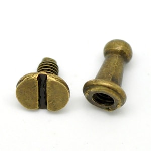 May include: Two antique brass screw-on fasteners, one with a round head and the other with a flat head. The fasteners are used for attaching fabric or leather to a surface.