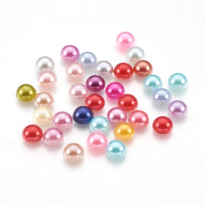 May include: A collection of colorful, round beads in various shades including pink, red, blue, and yellow. These small, semi-spherical beads are scattered across a white surface, ideal for jewelry making or craft projects.