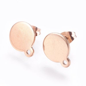 May include: A pair of rose gold stud earrings with a round disc shape and a small loop on the bottom.