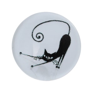 Può includere: Un cabochon di vetro ovale bianco con una silhouette nera di un gatto con la coda arrotolata. Il gatto è seduto su una superficie bianca.