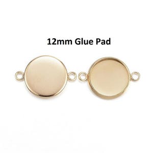 May include: Two gold-colored, round glue pads with a 12mm diameter. Each pad has a circular base and small loops on either side for attaching to other components. The text "12mm Glue Pad" is above the pads.