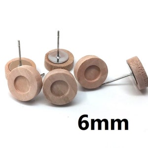 May include: Five wooden earring blanks with a 6 mm diameter hole in the center. The blanks are light brown and have a smooth finish. The earring posts are made of silver metal.