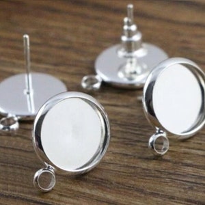 May include: Two silver earring settings with a round glass bezel. The settings have a post and a loop for attaching a charm or pendant.