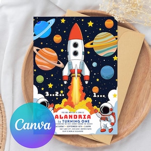 Op de afbeelding: Een kleurrijke uitnodiging met een ruimtethema. Het toont een opstijgende raket, planeten, sterren en een astronaut. De tekst luidt "ALANDRIA is TURNING ONE" met evenementdetails. De uitnodiging ligt op een houten dienblad met een envelop.