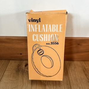 May include: A vintage orange box with the words "vinyl INFLATABLE CUSHION" in white lettering. The box features a circular inflatable cushion illustration with the brand name "DAVOL". The product number is 3556.