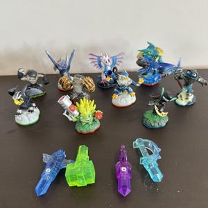 May include: A selection of colourful Skylanders action figures, showcasing diverse characters with distinctive designs and poses. The figures are plastic and have detailed features, including wings, weapons, and accessories. Some figures are on cloud or rock bases.