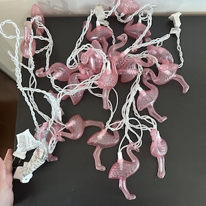 Puede incluir: Cadena de luces con flamencos rosas y cable blanco. Las luces de flamenco son de plástico rosa translúcido. Las luces están enchufadas a una toma de corriente estándar.