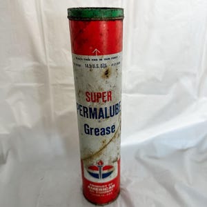 Puede incluir: Lata de grasa Super Permalube vintage. La lata cilíndrica tiene la parte superior e inferior rojas con un borde verde. El cuerpo es blanco con texto rojo y azul y un logotipo. La lata pesa 411 gramos.