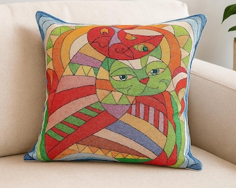 May include: Square throw pillow with a colorful cat design. The pillow features a vibrant, geometric pattern with a green cat and a red cat, outlined in black. The border is a solid blue.