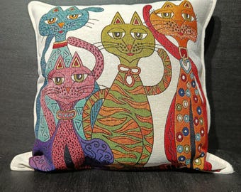 May include: Decorative square pillow featuring a whimsical design of four stylized cats. The cats are in various colors, including blue, green, orange, and pink, with intricate patterns and details. The pillow has a white border and is likely made of a woven fabric.