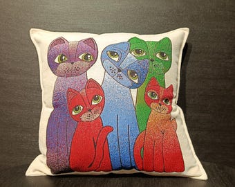 May include: A decorative square pillow featuring a colorful cat design. The pillow showcases five stylized cats in shades of purple, blue, green, and red, each with large, expressive eyes. The cats are set against a white background.