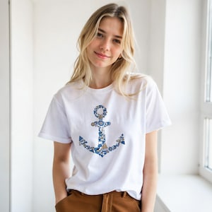 Puede incluir: Camiseta blanca con un dise&ntilde;o de ancla azul y blanco. El ancla est&aacute; compuesta por elementos n&aacute;uticos. La camiseta tiene mangas cortas y cuello redondo. El tema general es n&aacute;utico y mar&iacute;timo.