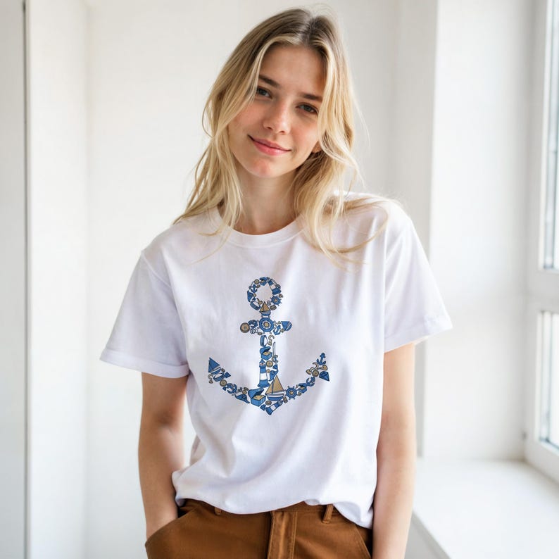 Puede incluir: Camiseta blanca con un dise&ntilde;o de ancla azul y blanco. El ancla est&aacute; compuesta por elementos n&aacute;uticos. La camiseta tiene mangas cortas y cuello redondo. El tema general es n&aacute;utico y mar&iacute;timo.
