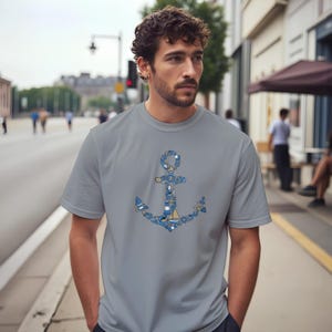 Puede incluir: Una camiseta gris con un dise&ntilde;o de ancla detallado. El ancla est&aacute; compuesta por varios elementos n&aacute;uticos en tonos azules y blancos. La camiseta es una prenda casual para el d&iacute;a a d&iacute;a.