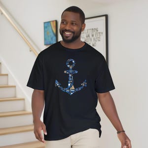Puede incluir: Camiseta negra con un dise&ntilde;o de ancla azul compuesto por elementos n&aacute;uticos como barcos y timones. El ancla est&aacute; centrada en la camiseta, con un patr&oacute;n detallado. La camiseta es de manga corta y parece estar hecha de un material suave.