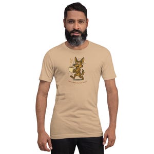 May include: Tan t-shirt featuring a cartoon coyote holding a steaming coffee cup. The coyote is brown with yellow accents and a smiling expression. The text "Java Jumpstarted Coyote" is below the graphic.