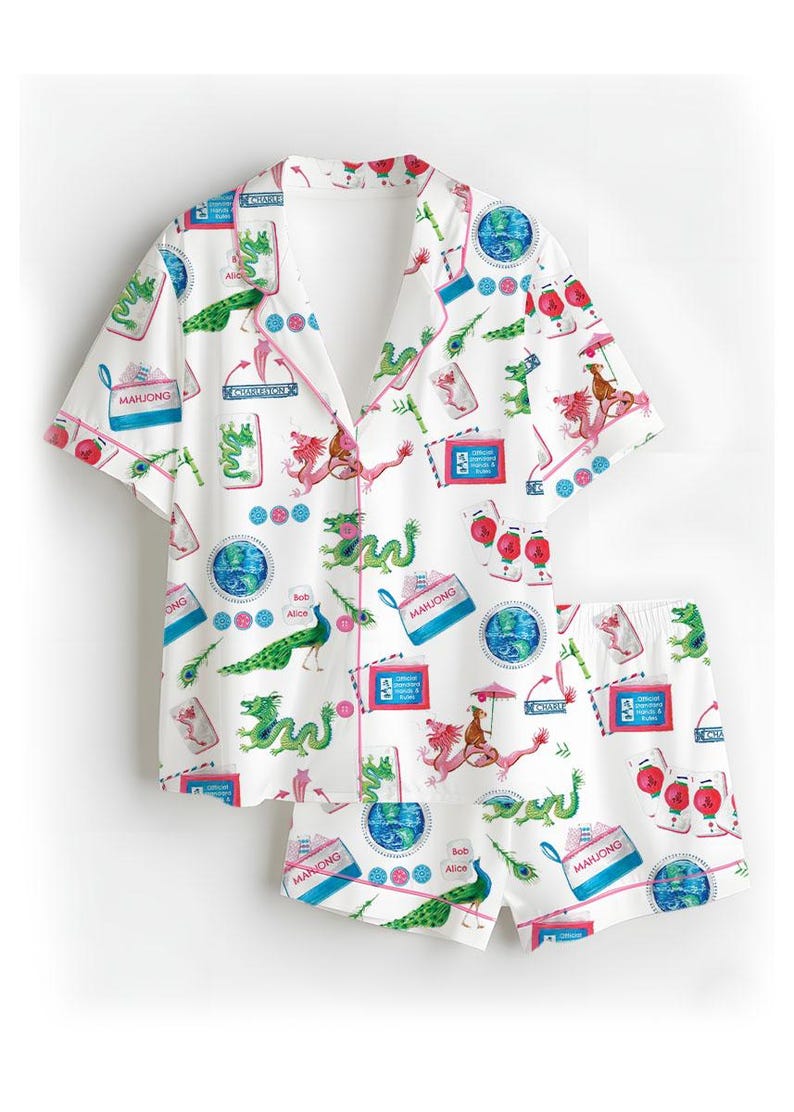 Puede incluir: Conjunto de pijama blanco con un estampado caprichoso con dragones, pavos reales y fichas de Mahjong. La parte superior de manga corta y los pantalones cortos tienen ribetes rosas y una parte delantera abotonada. La impresi&oacute;n incluye el texto "Mahjong" y "Bob & Alice".
