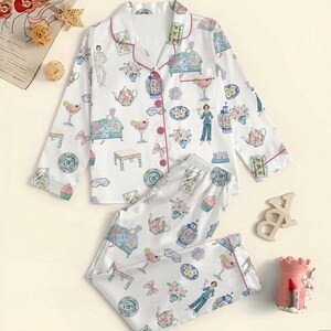 May include: A white long-sleeve pajama set with a button-down top and matching pants, featuring a colorful repeating print of people, teapots, cocktails, furniture, and floral arrangements, accented with thin pink piping along the edges.