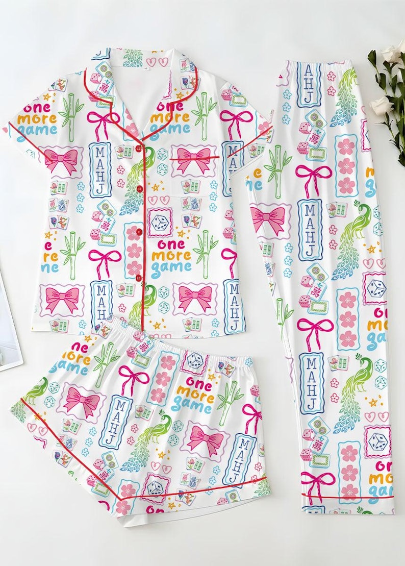 May include: A white pajama set featuring a short-sleeved button-down top, shorts, and long pants. The fabric has a colorful print of pink bows, green bamboo, dice, peacocks, and the text "one more game" and "MAHJ" in blue and red.