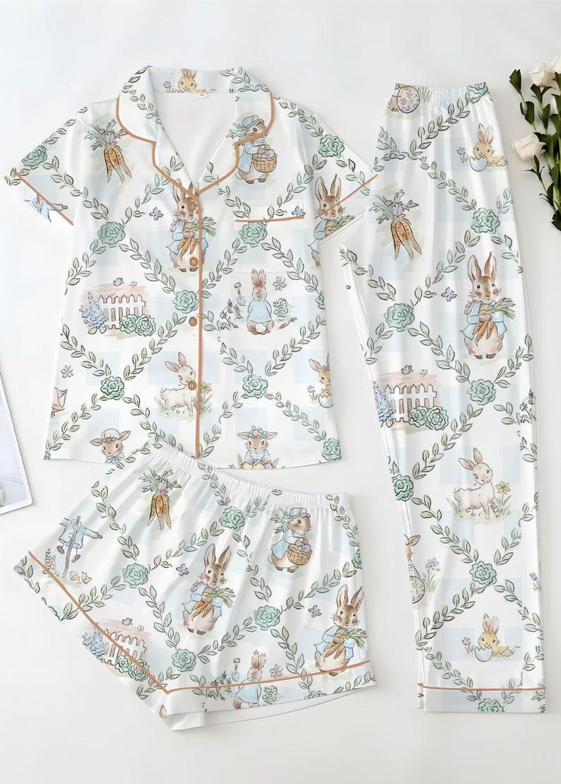 Puede incluir: Conjunto de pijama blanco con estampado de conejitos. El conjunto incluye una camisa de manga corta con botones, pantalones cortos y pantalones largos. El estampado de conejitos presenta conejos, zanahorias y elementos florales. El ribete es de color marr&oacute;n claro.