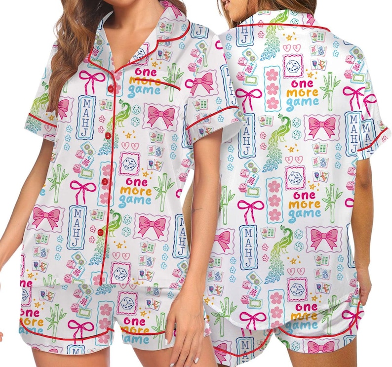 May include: A white pajama set with short sleeves and shorts featuring a red piped trim. The fabric has a colorful pattern of pink bows, green bamboo stalks, dice, peacocks, and the text "one more game" and "MAHJ" in blue and pink.
