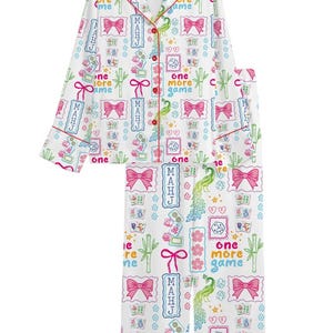 May include: A white long-sleeve pajama set with a button-down top and matching pants. The fabric features a colorful pattern of pink bows, green bamboo stalks, green peacocks, dice, and the text "one more game" and "MAHJ" in various colors.