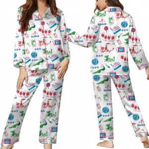Puede incluir: Conjunto de pijama de sat&eacute;n blanco con un estampado colorido con dragones, pavos reales y otros dise&ntilde;os caprichosos. El conjunto incluye una camisa abotonada de manga larga y pantalones a juego, ribeteados con ribetes rosas.