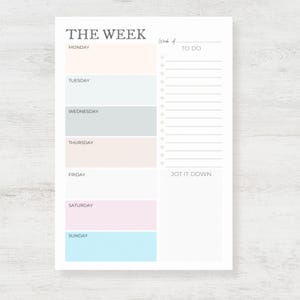 May include: A weekly planner with pastel-colored blocks for each day of the week. The top of the page reads "THE WEEK" in a serif font. There is a section for "TO DO" and "JOT IT DOWN" on the right side of the page.