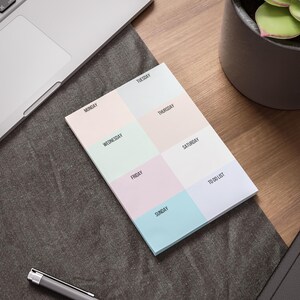 May include: A pastel-colored weekly planner notepad with sections for each day of the week and a to-do list. The notepad is on a wooden desk next to a laptop and a pen.